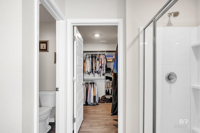 bathroom featuring a shower stall, toilet, a walk in closet, and wood finished floors