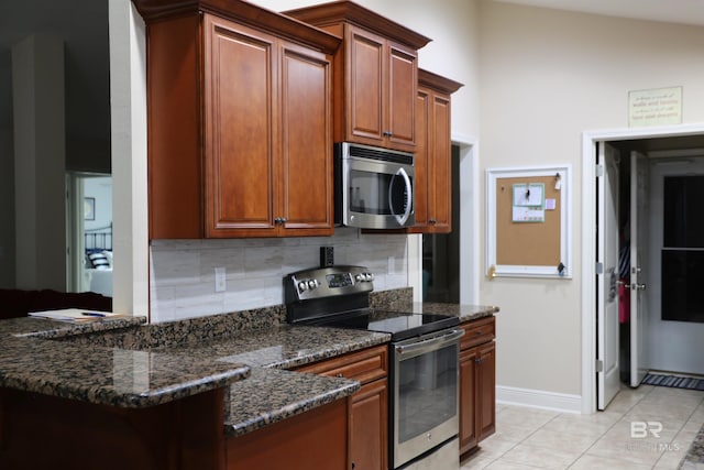 kitchen with light tile patterned floors, decorative backsplash, dark stone countertops, appliances with stainless steel finishes, and a peninsula