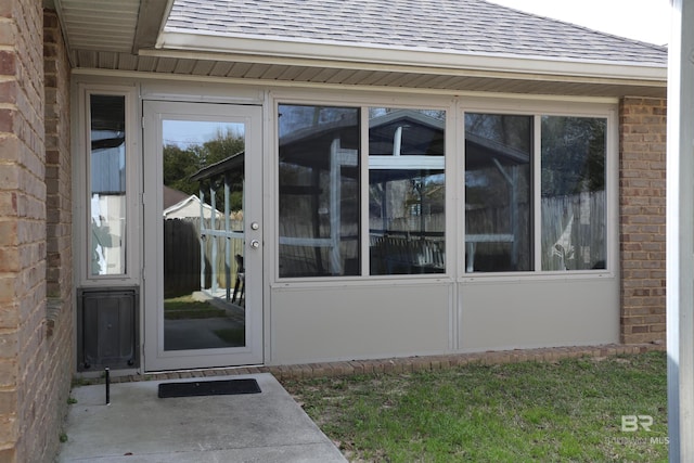 doorway to property with brick siding and a shingled roof