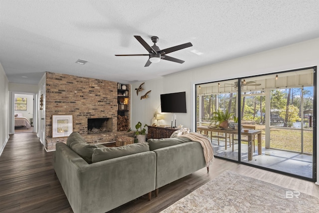 living room with ceiling fan, a textured ceiling, a brick fireplace, and wood finished floors