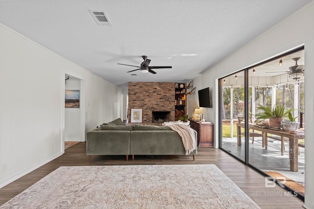 living room featuring visible vents, a ceiling fan, wood finished floors, a textured ceiling, and a fireplace