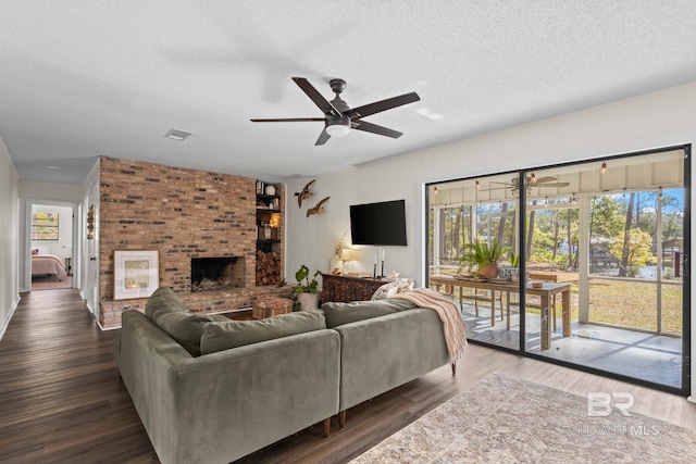 living area featuring a textured ceiling, wood finished floors, visible vents, a ceiling fan, and a brick fireplace