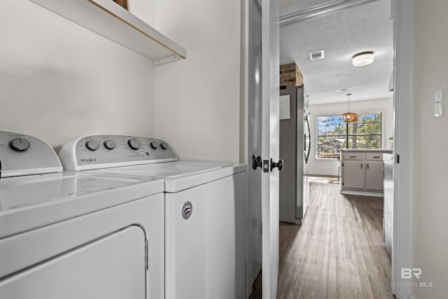 washroom featuring a textured ceiling, laundry area, wood finished floors, visible vents, and independent washer and dryer