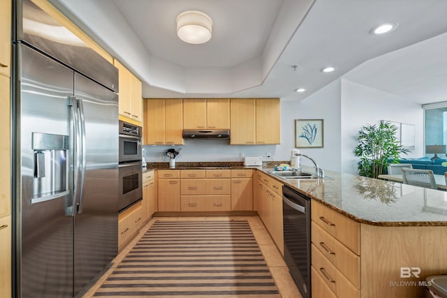 kitchen featuring sink, stone counters, appliances with stainless steel finishes, light brown cabinetry, and kitchen peninsula