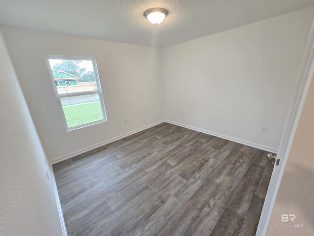 empty room with a textured ceiling, dark wood finished floors, and baseboards