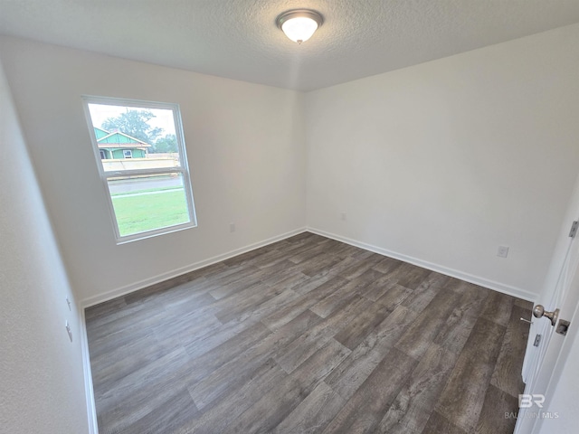 empty room featuring a textured ceiling, dark wood finished floors, and baseboards