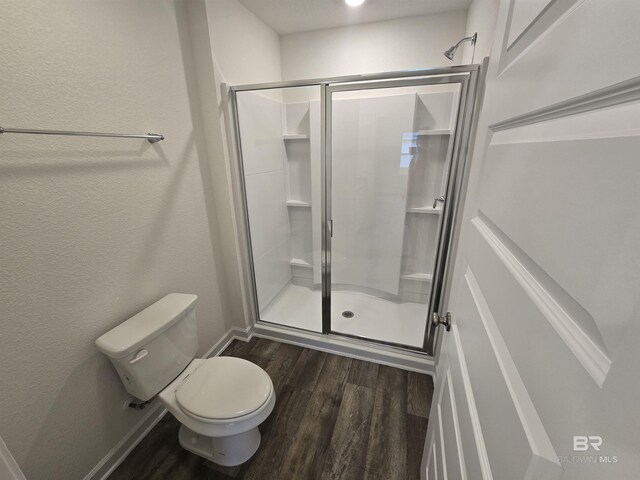 bathroom with toilet, a shower stall, baseboards, and wood finished floors