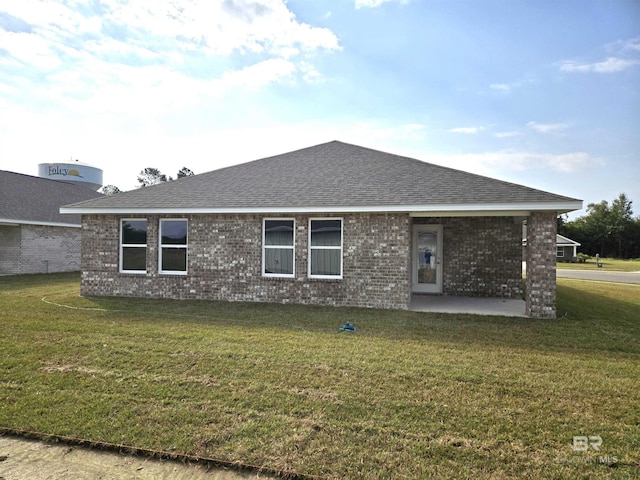 back of property featuring brick siding, a lawn, a patio area, and a shingled roof