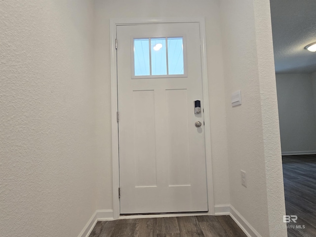 doorway to outside featuring a textured wall, dark wood finished floors, and baseboards