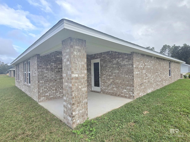 view of home's exterior with brick siding, a yard, and a patio