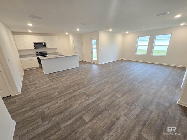 kitchen with appliances with stainless steel finishes, open floor plan, white cabinets, a sink, and an island with sink