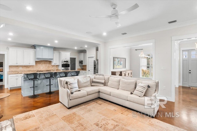 living room with ceiling fan with notable chandelier and ornamental molding