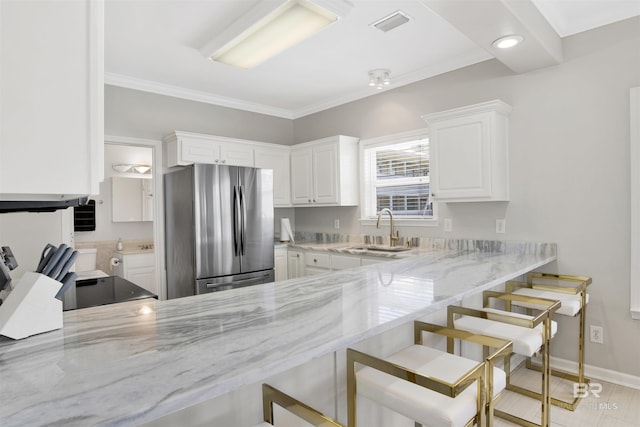 kitchen featuring a peninsula, a sink, light stone counters, a kitchen breakfast bar, and freestanding refrigerator