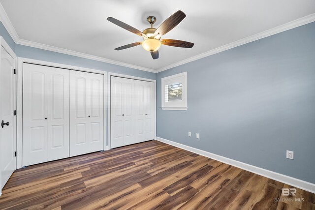 unfurnished bedroom with baseboards, a ceiling fan, dark wood-style floors, crown molding, and two closets