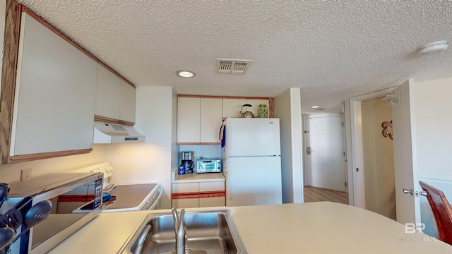 kitchen with white fridge, a textured ceiling, range, and white cabinets