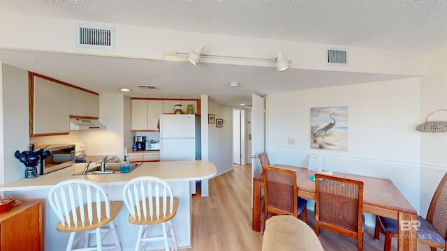 kitchen with a textured ceiling, white refrigerator, light hardwood / wood-style flooring, and sink