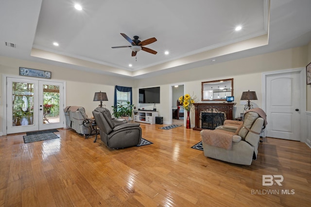 living room with french doors, a raised ceiling, ceiling fan, and light hardwood / wood-style floors