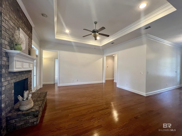 unfurnished living room with a tray ceiling, a brick fireplace, visible vents, and dark wood finished floors