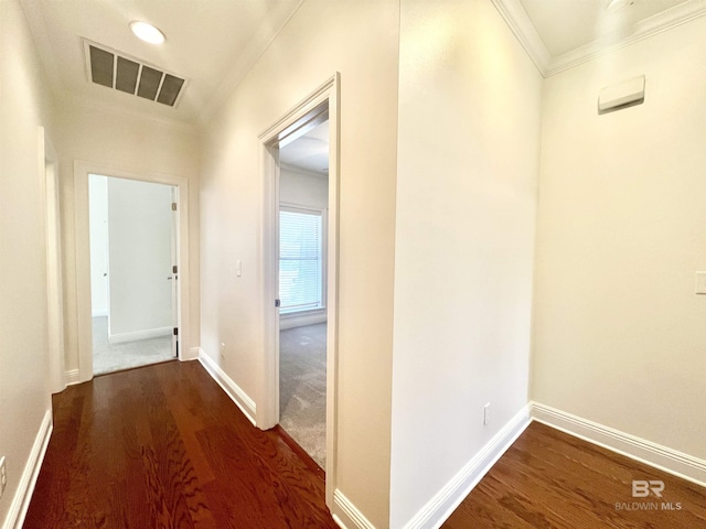 corridor featuring dark wood-type flooring, visible vents, crown molding, and baseboards