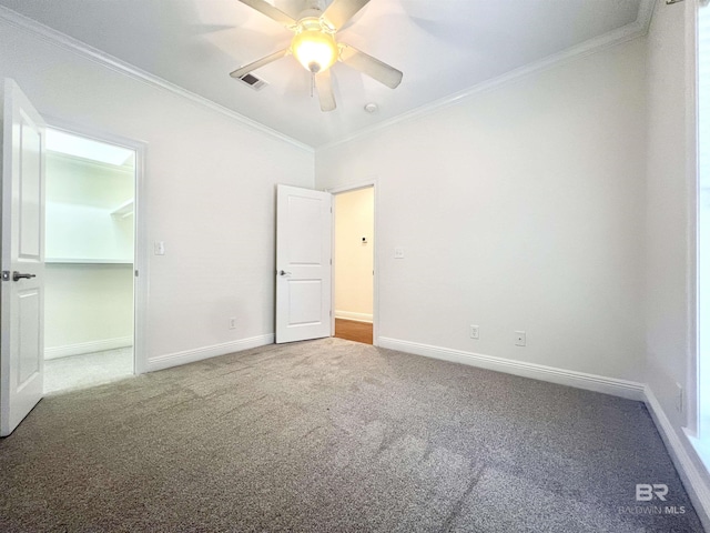 unfurnished bedroom featuring visible vents, baseboards, ornamental molding, carpet, and a walk in closet