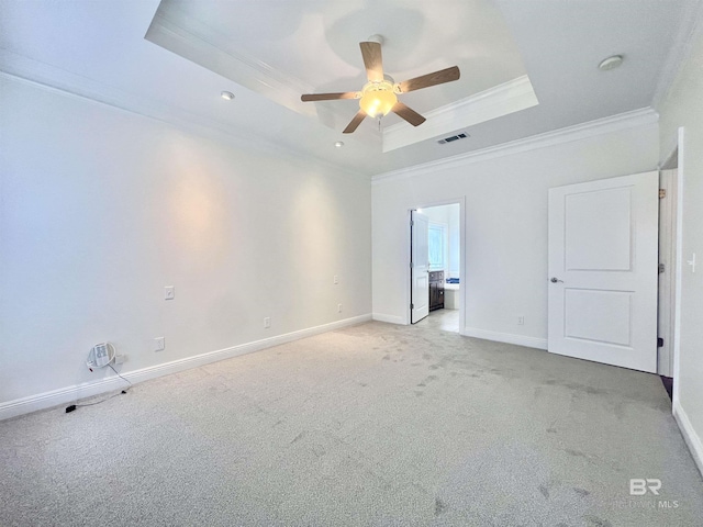 empty room featuring a raised ceiling, light colored carpet, visible vents, ornamental molding, and baseboards