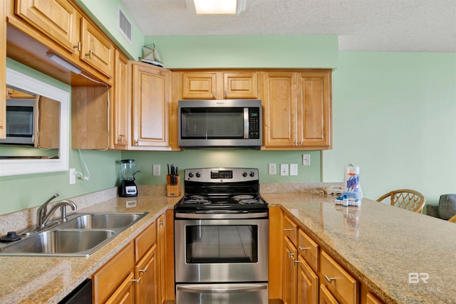 kitchen with appliances with stainless steel finishes, light stone counters, a textured ceiling, and sink