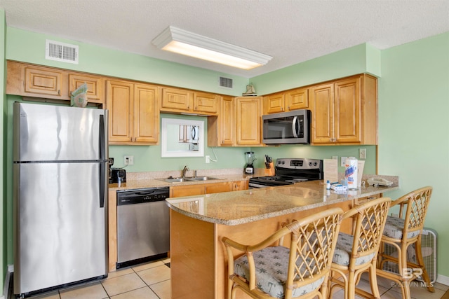 kitchen with a kitchen breakfast bar, light tile patterned floors, appliances with stainless steel finishes, kitchen peninsula, and light stone counters