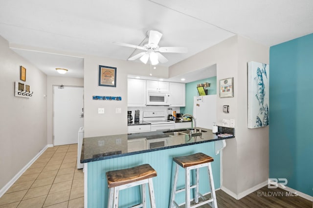 kitchen featuring kitchen peninsula, white appliances, a kitchen breakfast bar, white cabinets, and sink