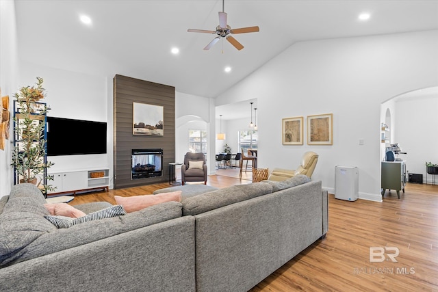 living room featuring a large fireplace, high vaulted ceiling, light wood-type flooring, and ceiling fan