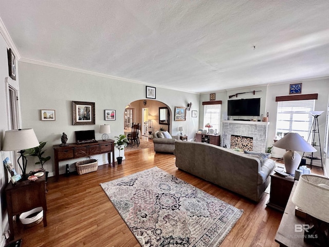 living room featuring hardwood / wood-style flooring, a fireplace, ornamental molding, and a textured ceiling