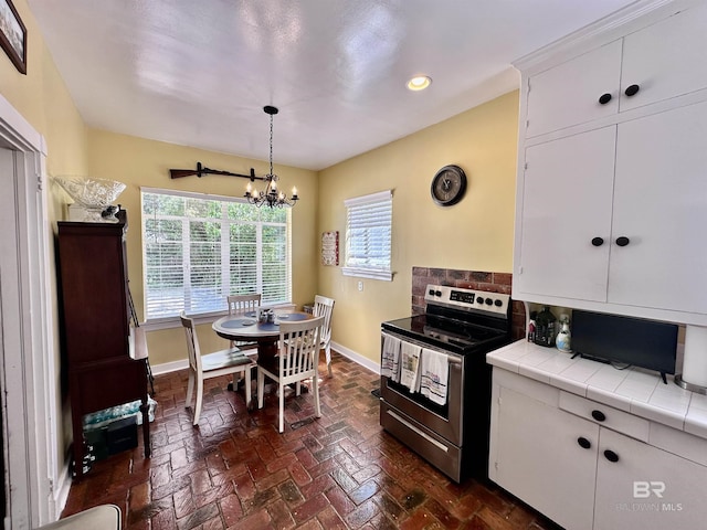 kitchen featuring a notable chandelier, tile countertops, decorative light fixtures, stainless steel electric stove, and white cabinets