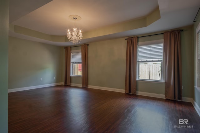 spare room featuring dark hardwood / wood-style flooring, an inviting chandelier, plenty of natural light, and a raised ceiling