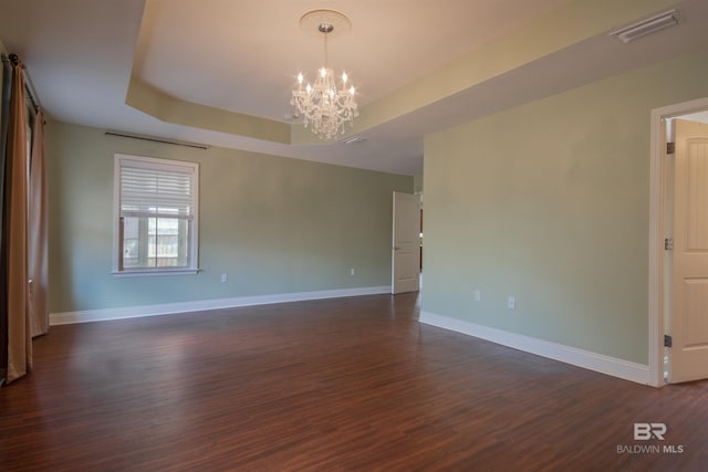 empty room featuring a notable chandelier, a tray ceiling, and dark wood-type flooring