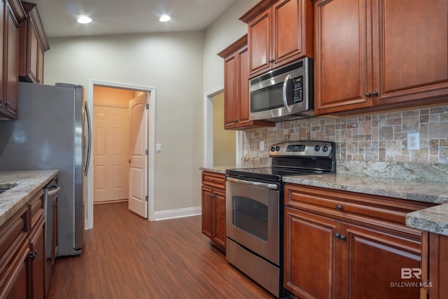 kitchen with stainless steel appliances, dark wood-type flooring, light stone counters, and backsplash