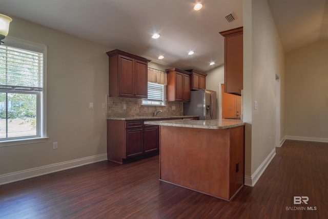 kitchen with vaulted ceiling, tasteful backsplash, light stone countertops, stainless steel fridge, and dark wood-type flooring