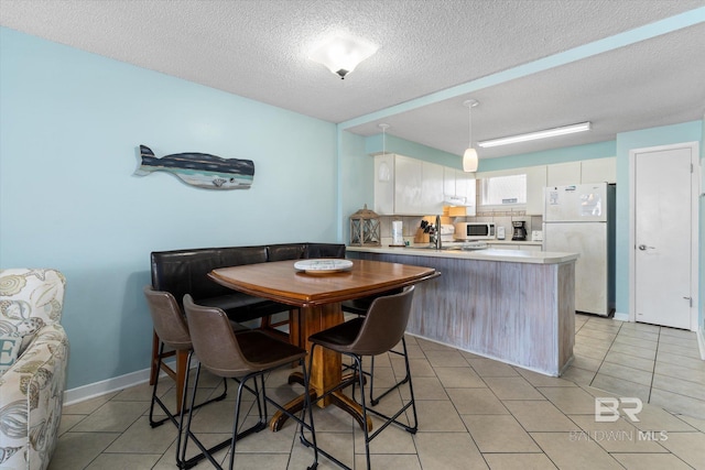 dining room with light tile patterned flooring, a textured ceiling, and baseboards