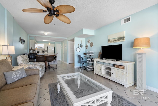 living area with a ceiling fan, light tile patterned floors, baseboards, and a textured ceiling