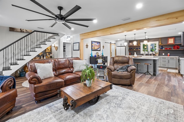 living room featuring hardwood / wood-style flooring, ceiling fan, a barn door, and beamed ceiling