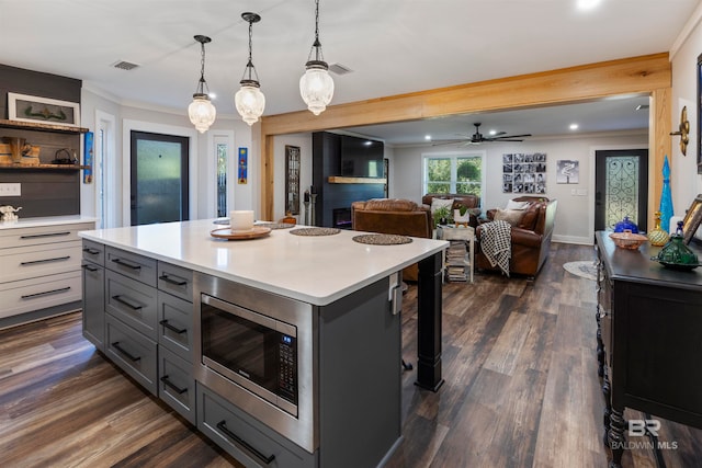 kitchen with pendant lighting, a breakfast bar, stainless steel microwave, a kitchen island, and dark hardwood / wood-style flooring