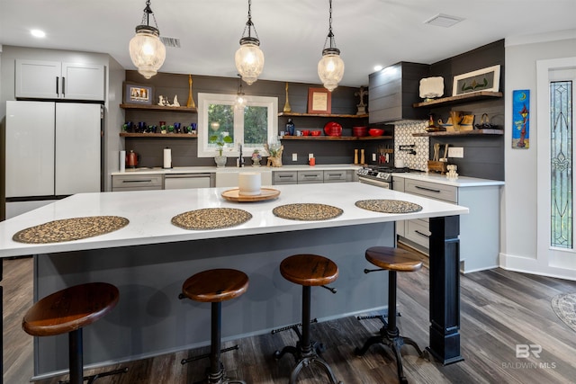 kitchen featuring hanging light fixtures, dark hardwood / wood-style flooring, decorative backsplash, a kitchen island, and appliances with stainless steel finishes