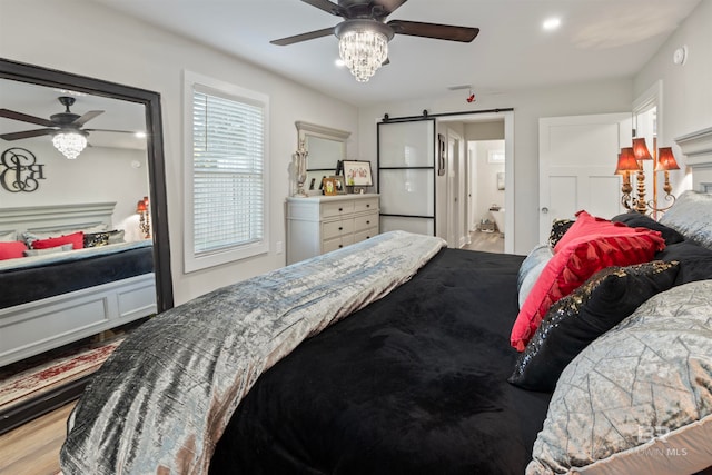 bedroom with a barn door, ceiling fan, ensuite bath, and light wood-type flooring