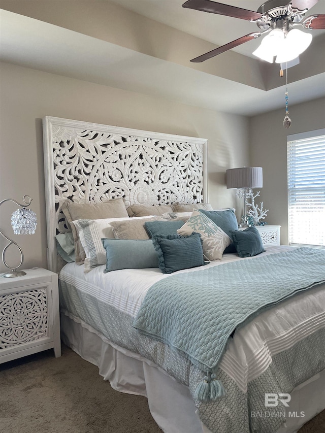 carpeted bedroom featuring a tray ceiling and a ceiling fan