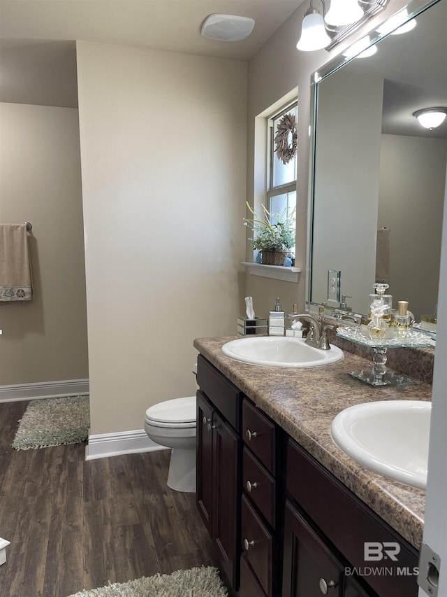 bathroom with double vanity, wood finished floors, a sink, and toilet