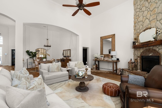 living room featuring ornamental molding, hardwood / wood-style flooring, ceiling fan, a fireplace, and a high ceiling