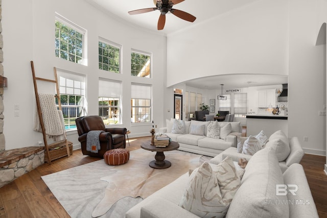 living room featuring a towering ceiling, dark wood-type flooring, ornamental molding, and ceiling fan