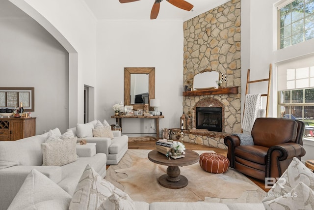 living room featuring crown molding, a towering ceiling, a stone fireplace, and ceiling fan