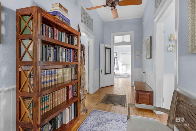 hallway with light wood finished floors, wainscoting, and visible vents