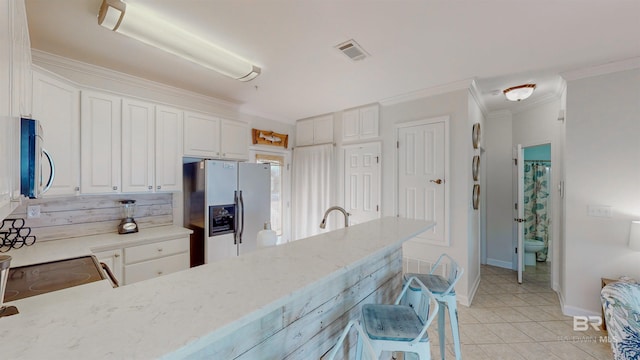 kitchen with light tile patterned floors, stainless steel appliances, light stone counters, ornamental molding, and white cabinets