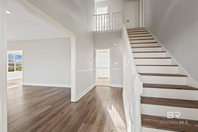 stairway with a high ceiling, baseboards, wood finished floors, and ornamental molding