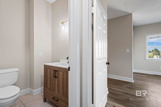 half bathroom with toilet, a textured ceiling, vanity, baseboards, and tile patterned floors